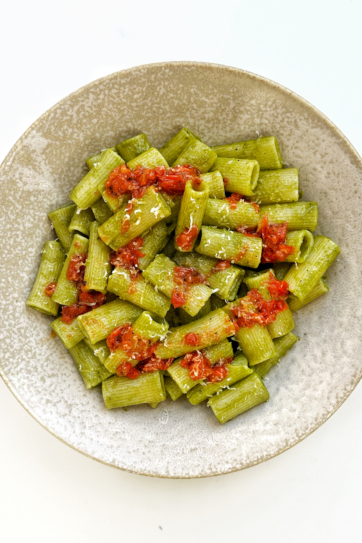 Green cilantro pasta topped with a paprika tomato dressing in a cream bowl on a white surface.