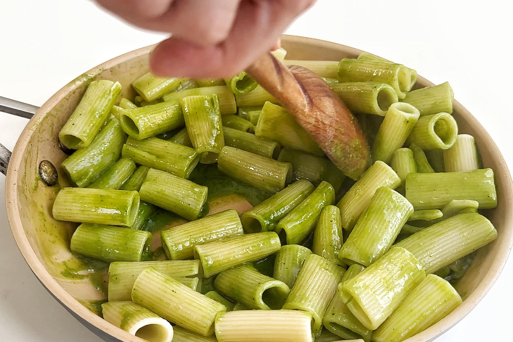 Combining rigatoni in with a cilantro pasta sauce in a frying pan.
