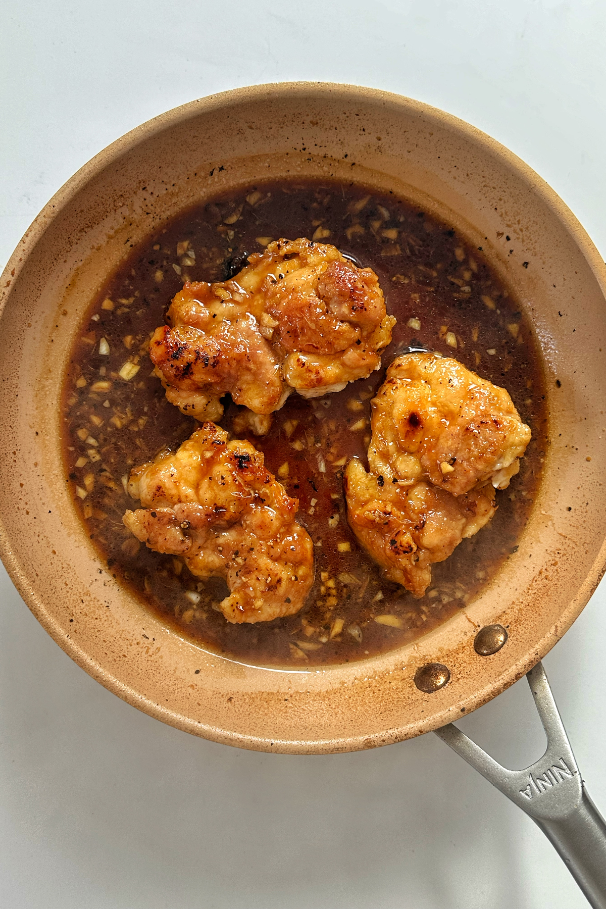 Frying chicken thighs in a honey ginger sauce in a frying pan.