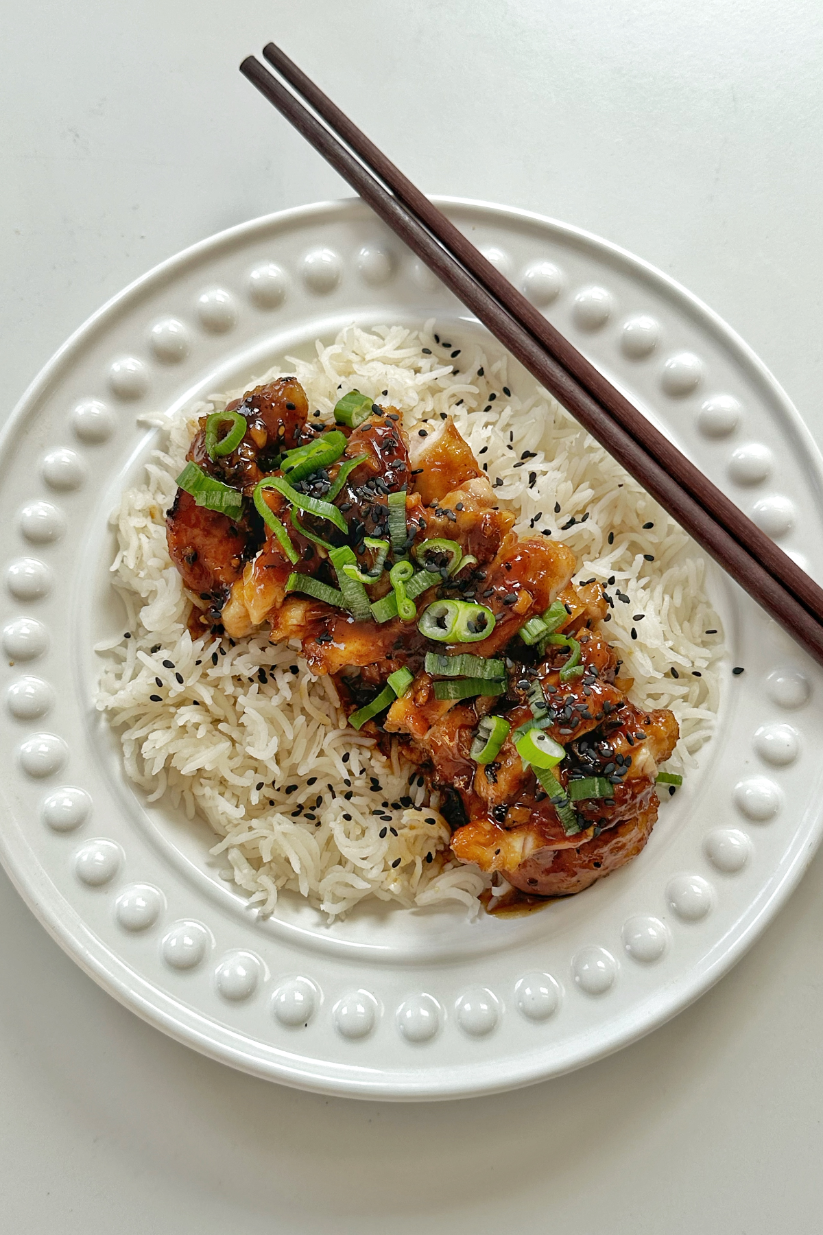 top down photo of honey ginger chicken with chopsticks on a white plate/bowl.