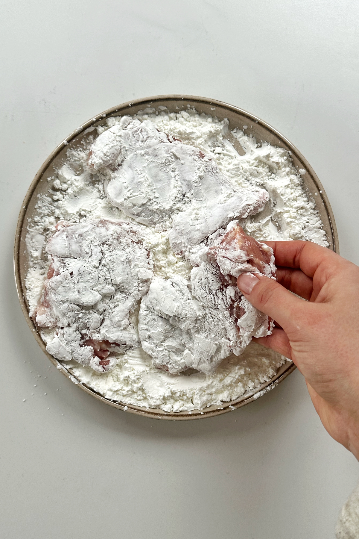 Dunking chicken thighs in cornstarch.