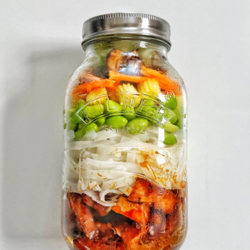 Jar of meal prep tofu with noodles and vegetables on a white background.