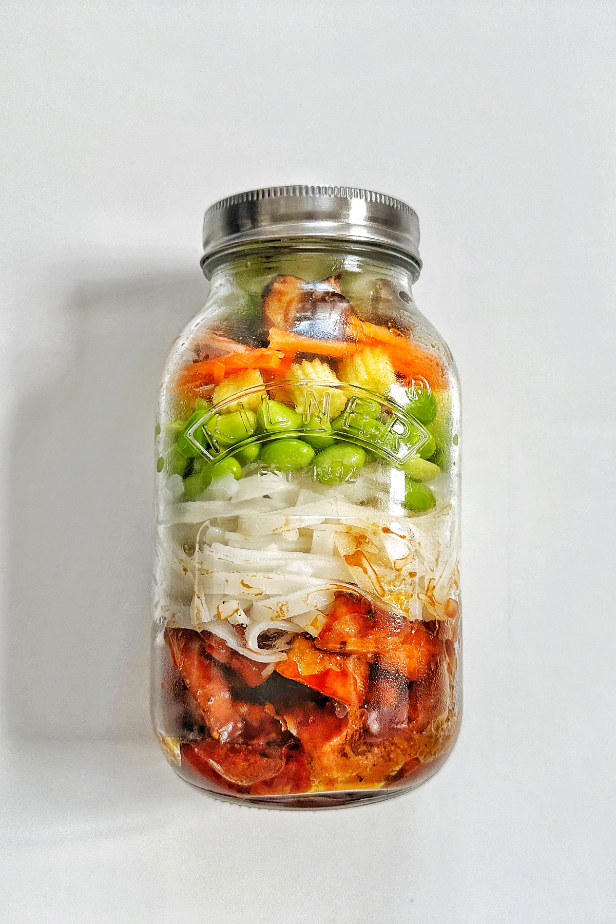 Jar of meal prep tofu with noodles and vegetables on a white background.