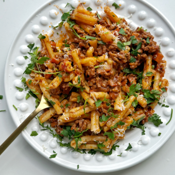 A bowl of casarecce bolognese with a fork in a white bowl.