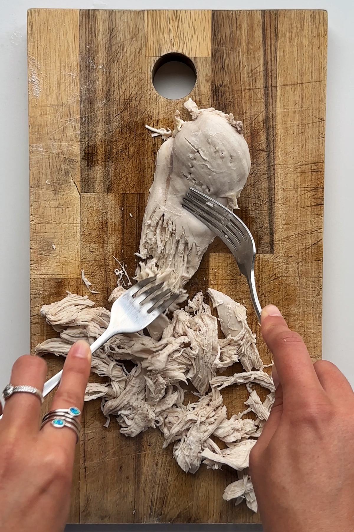 Shredding chicken with two forks on a wooden chopping board.