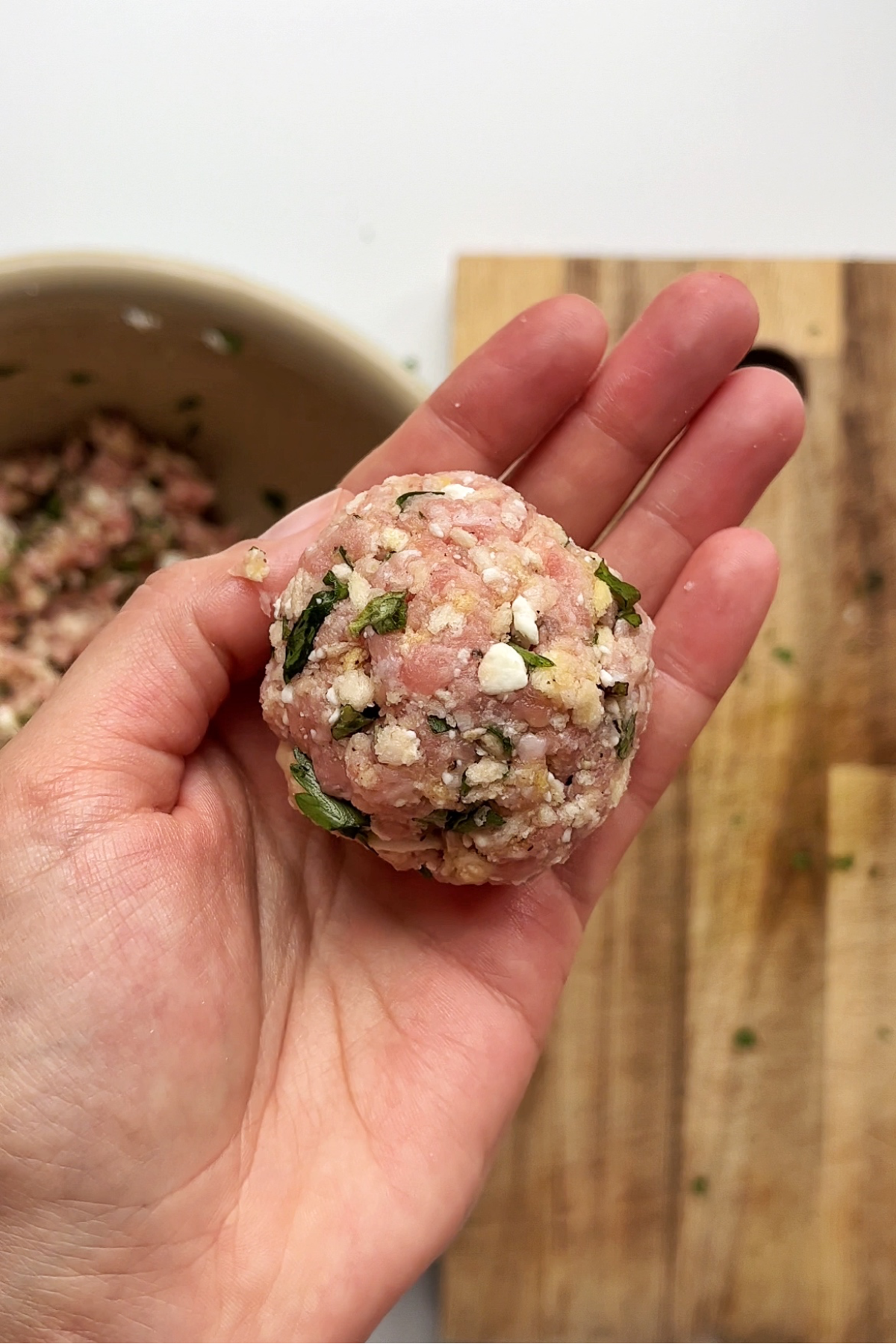 Uncooked formed meatball held in hand.