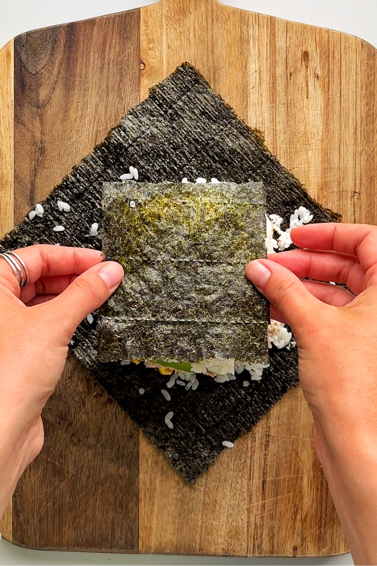 Placing a piece of nori on top of a sushi sandwich.