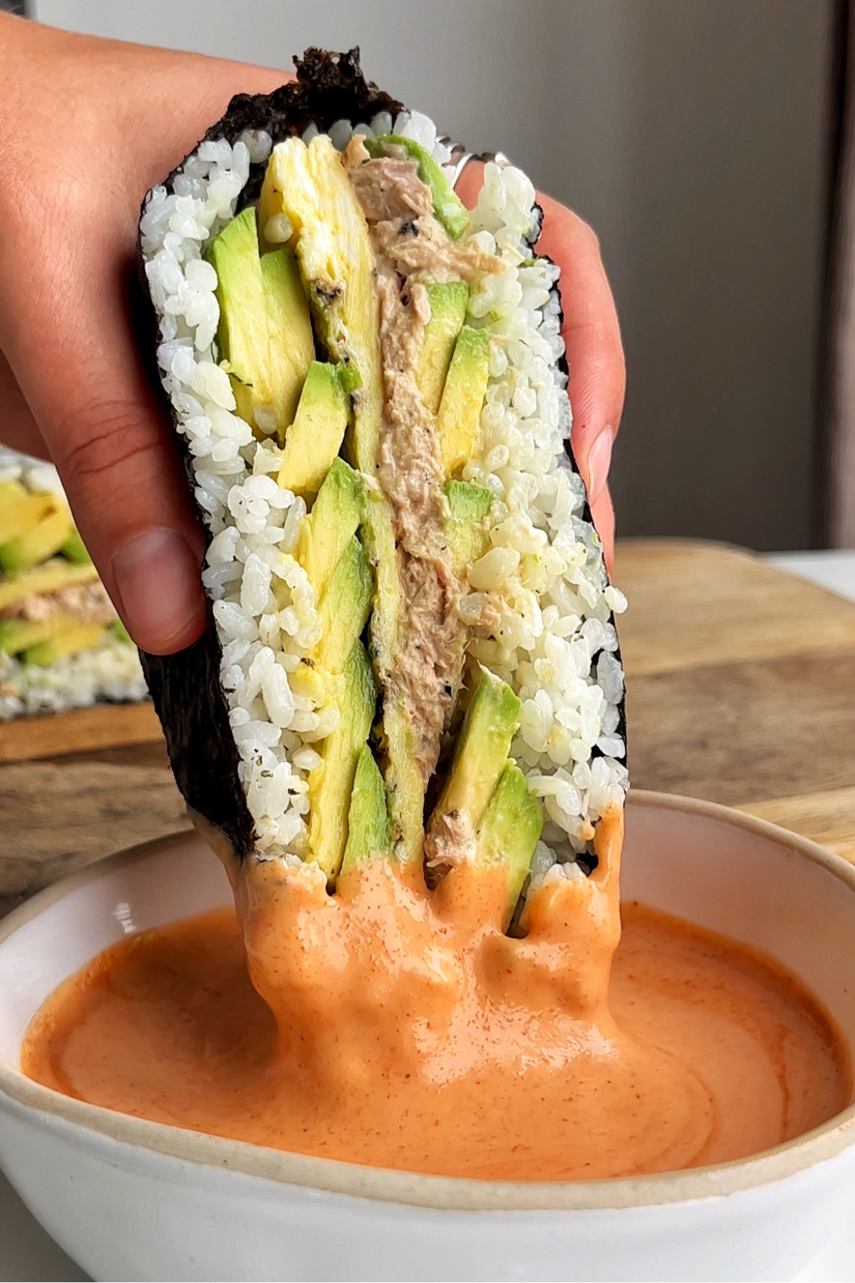 Onigirazu sushi sandwich being dipped in sriracha mayonnaise.