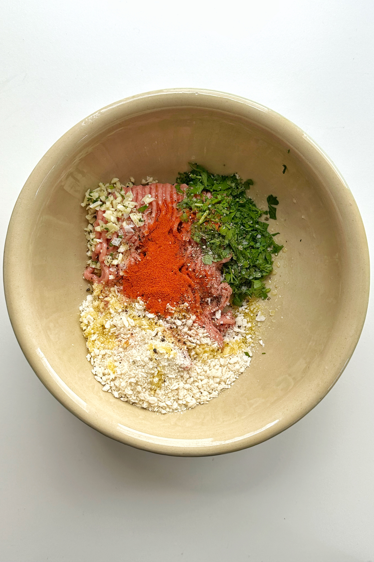 A large bowl containing ground turkey meat, paprika, parsley, breadcrumbs, and garlic.