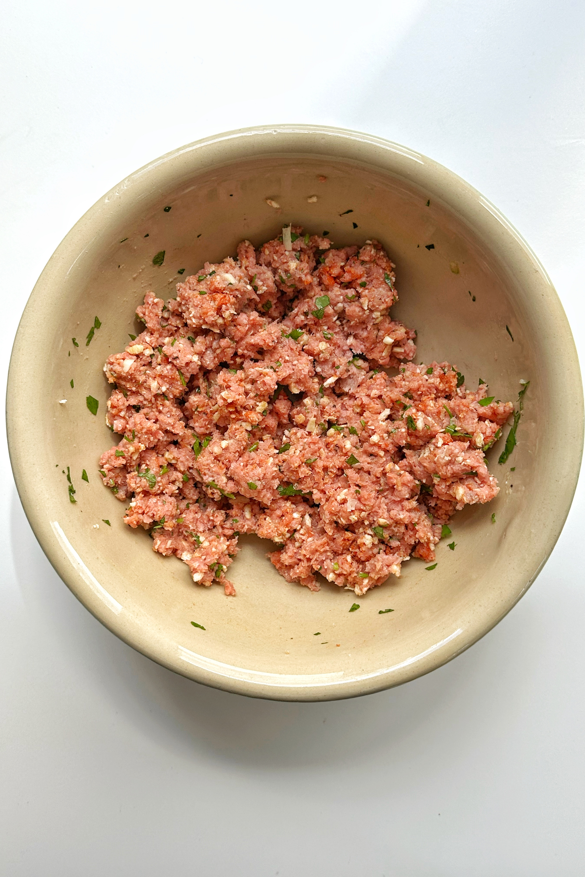 A large bowl containing combined ground turkey meat, parsley, garlic, breadcrumbs, and paprika.
