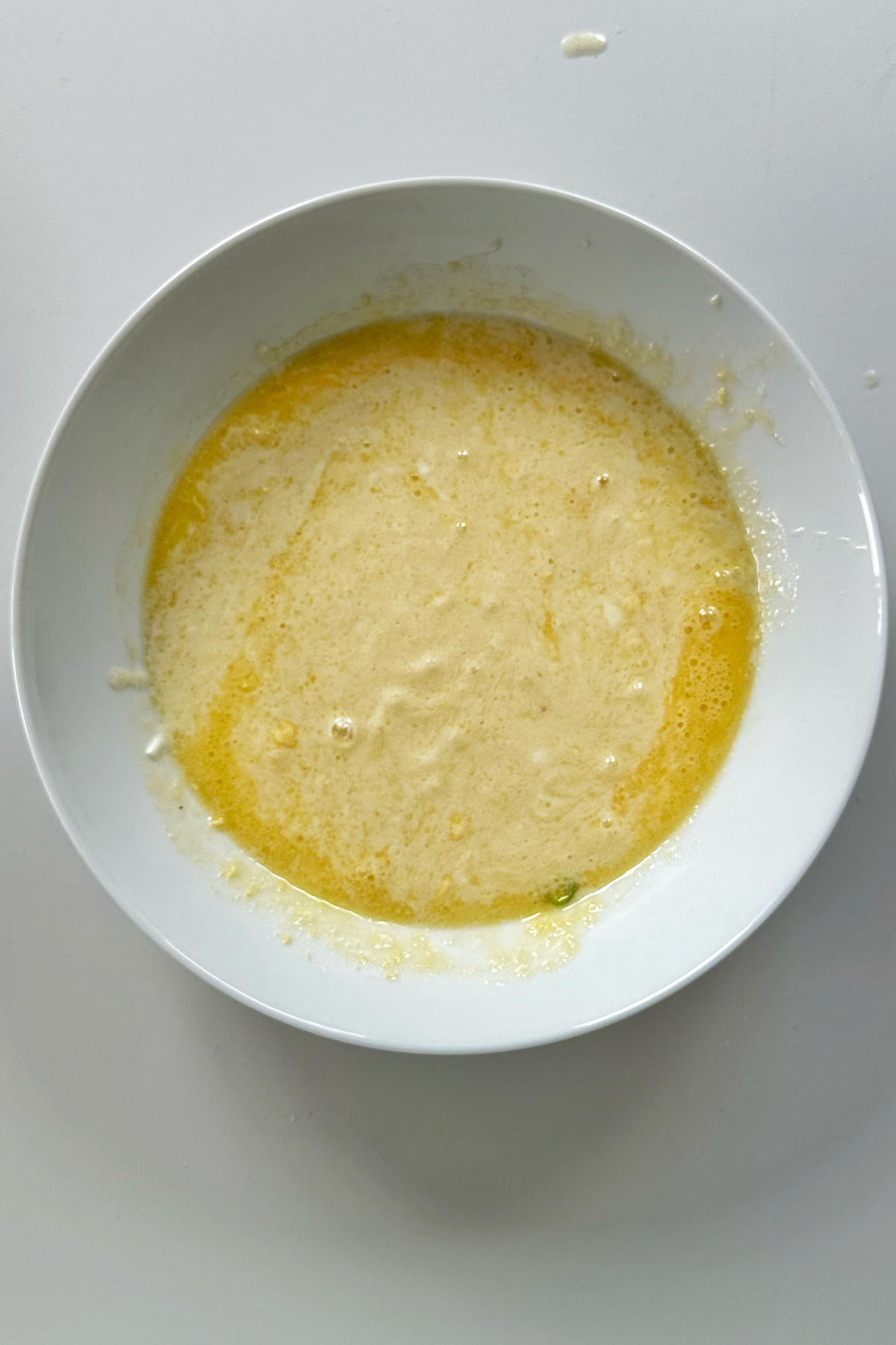 Combining the wet ingredients in a bowl for bacon and cheese muffins.