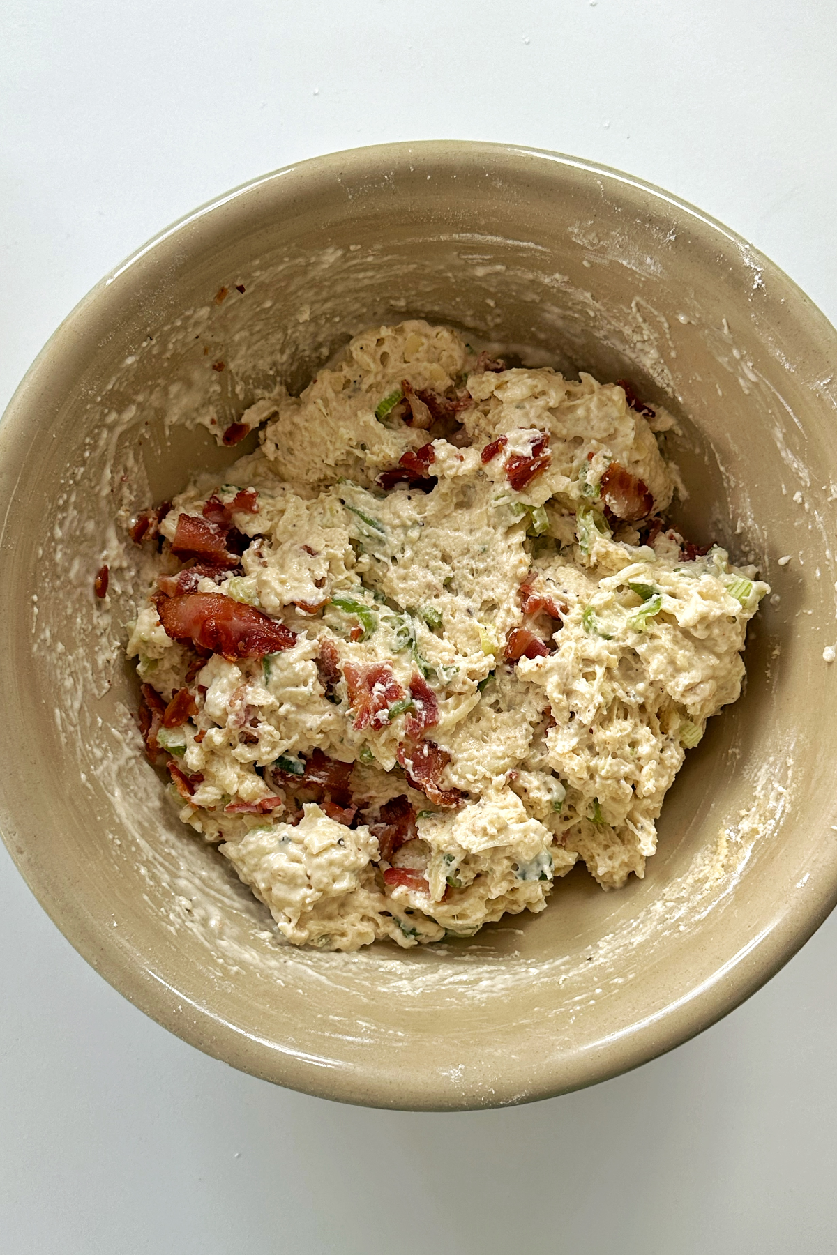 Combining the wet and dry ingredients with crispy bacon bits for savory muffins.