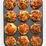 Bacon and cheese muffins in a baking tin on a white background.