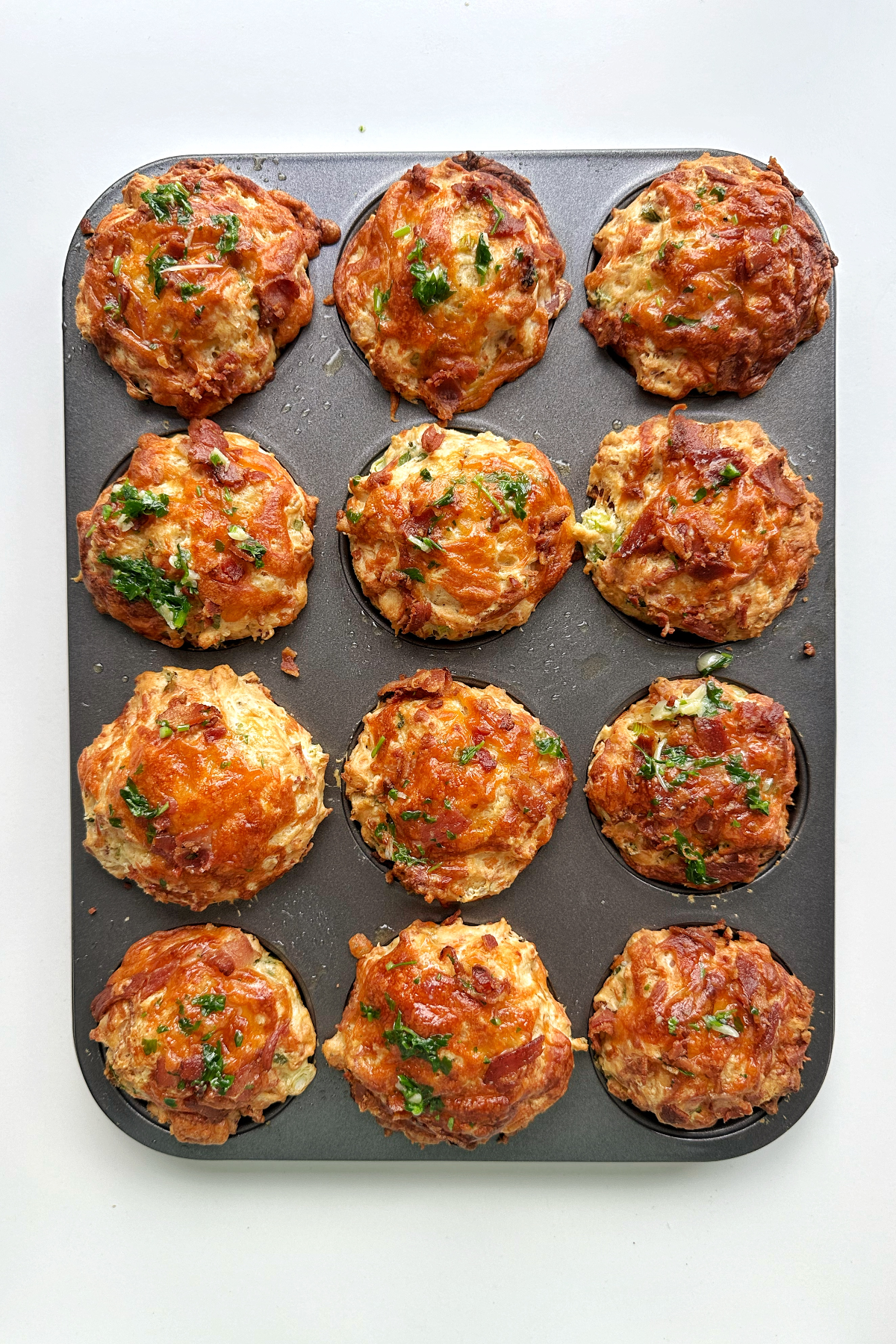 Bacon and cheese muffins in a baking tin on a white background.