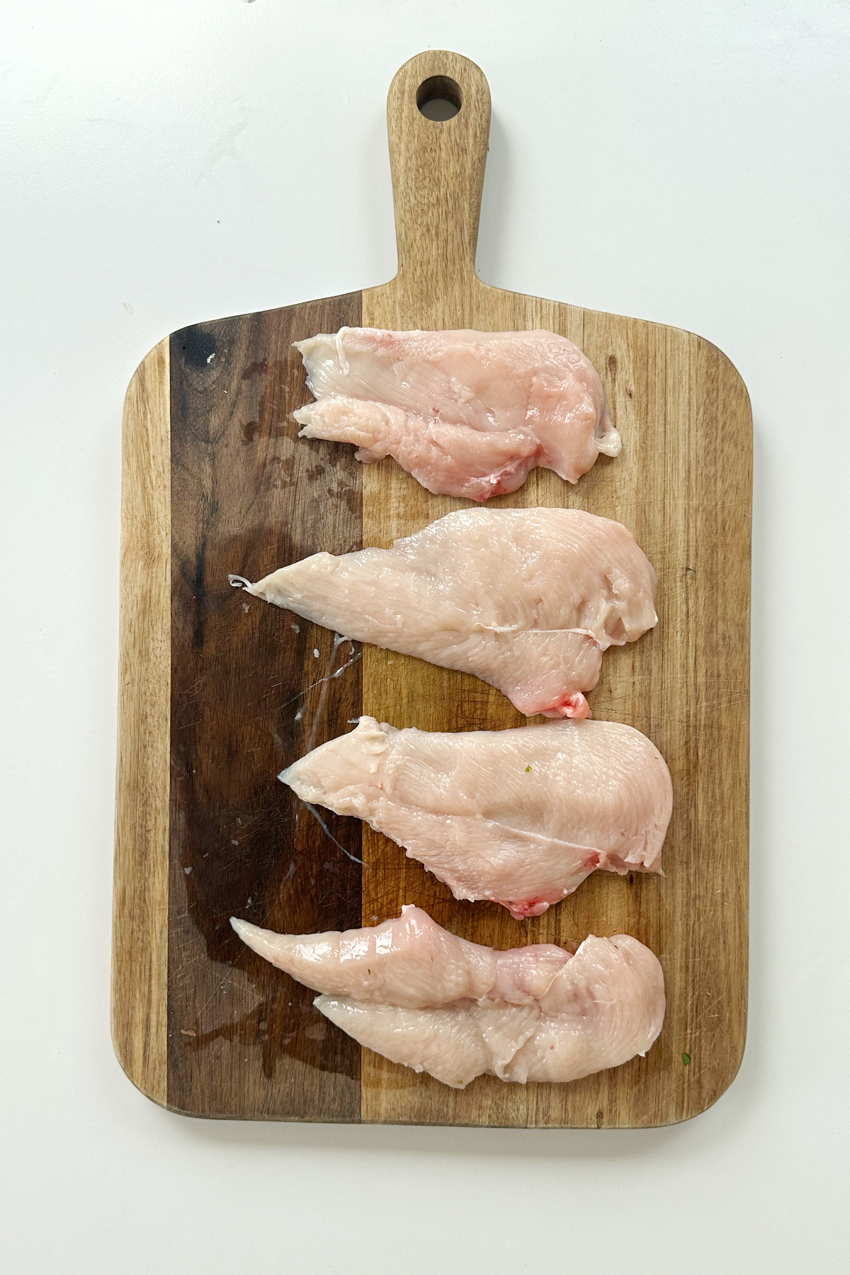 Slicing chicken breast horizontally and displayed on a wooden chopping board.