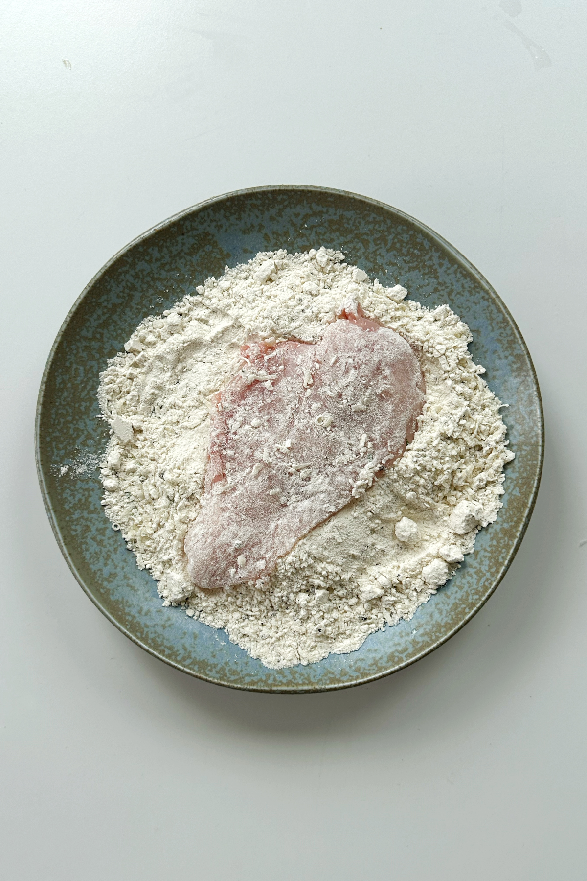 Coating chicken breast in a flour mixture of plain flour, parmesan, salt and pepper.