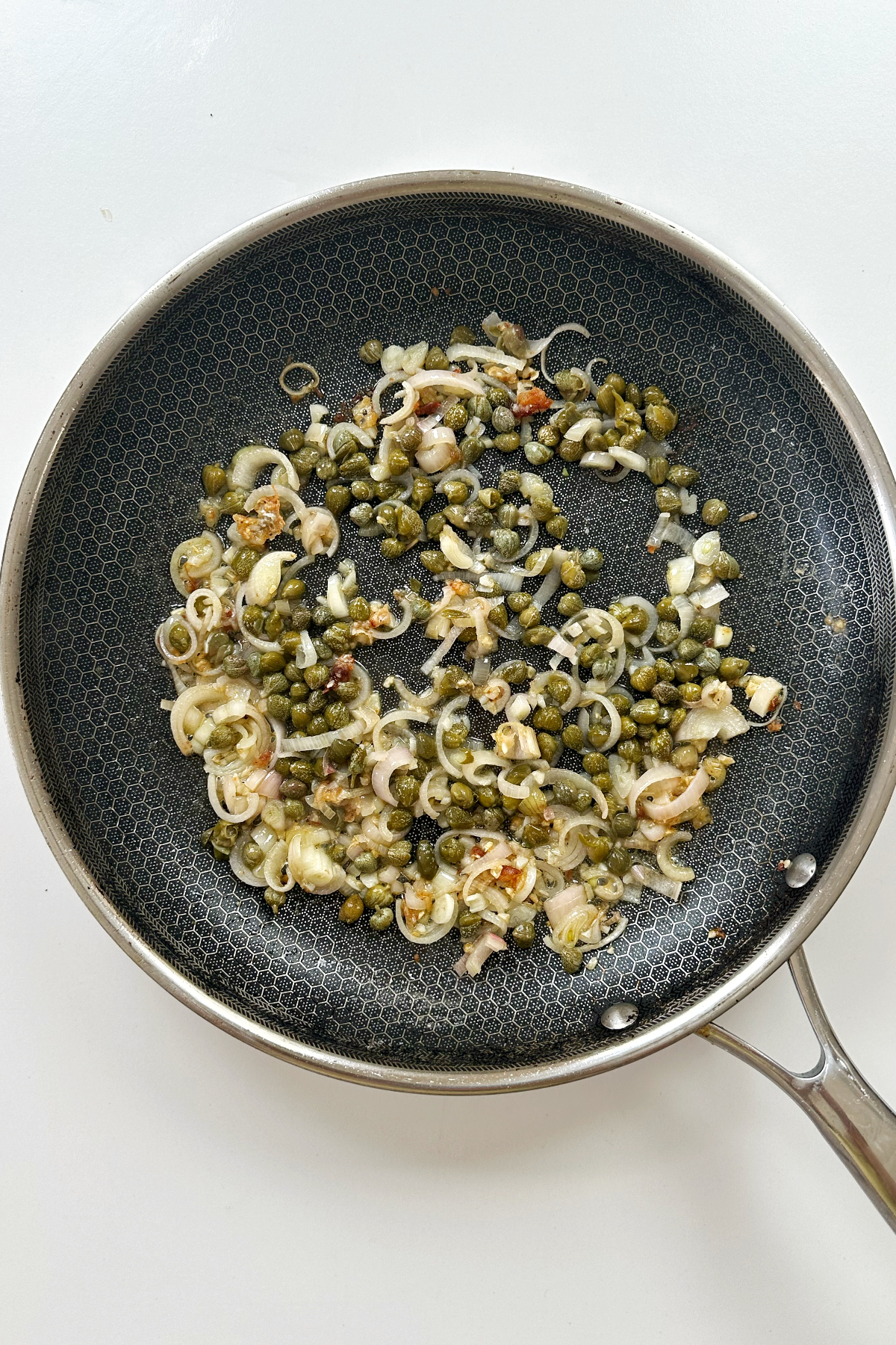 Frying shallots, garlic, and capers in a skillet with olive oil.