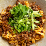 Close up of egg noodles with ground beef topped with cucumber, cilantro, and green onions.