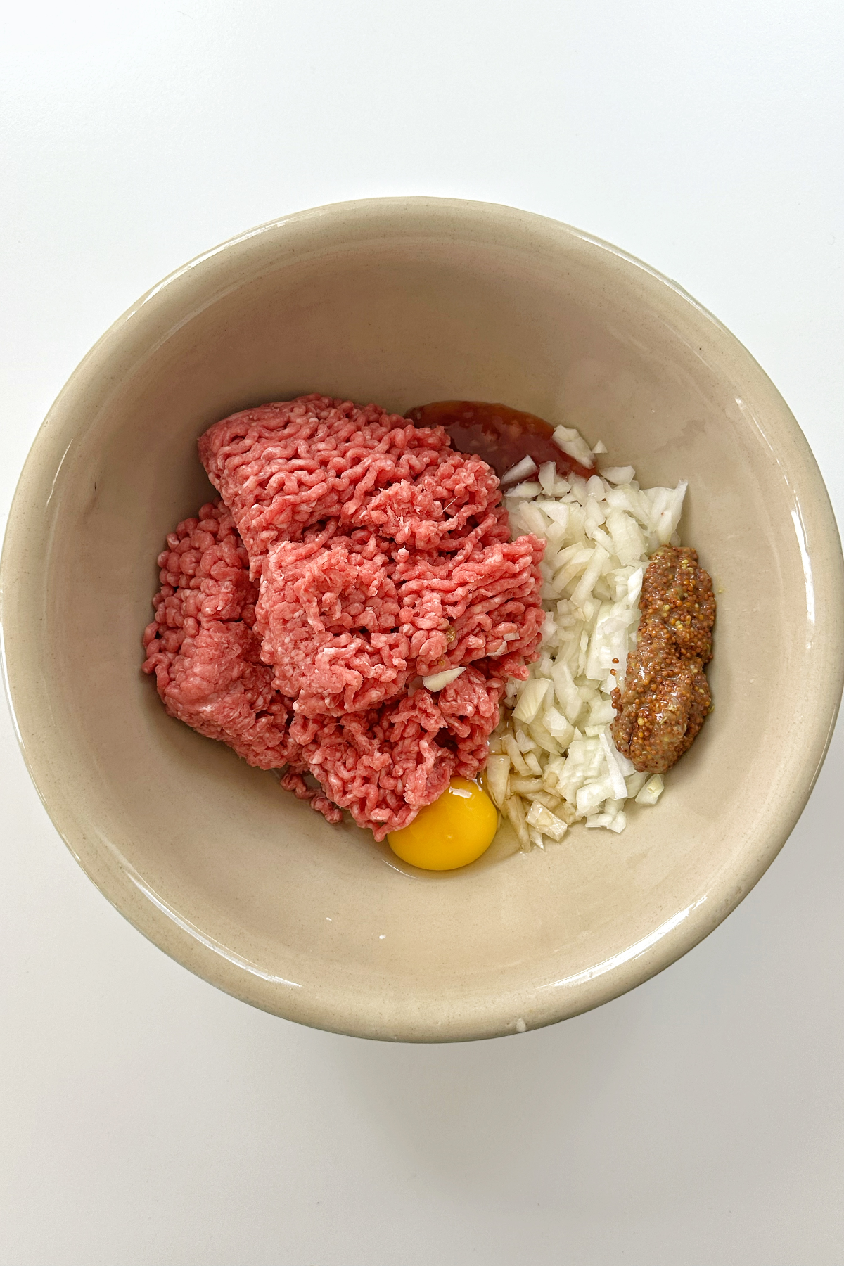 Ground beef, egg, onions, wholegrain mustard, and Worcestershire sauce in a large bowl making burger patties.