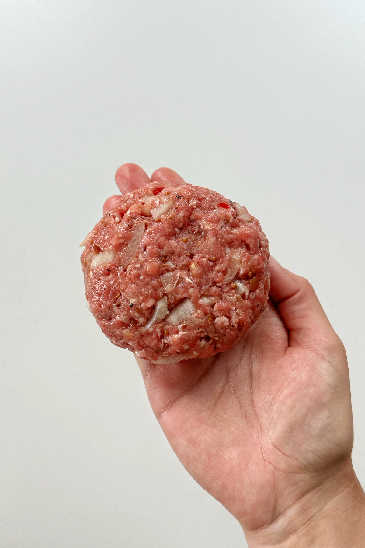 A homemade hamburger patty held out in a hand.
