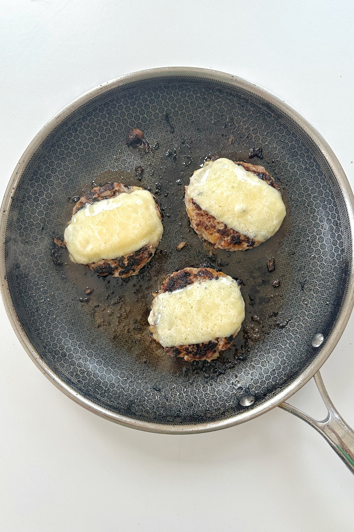 Frying hamburger patties layered with cheese.