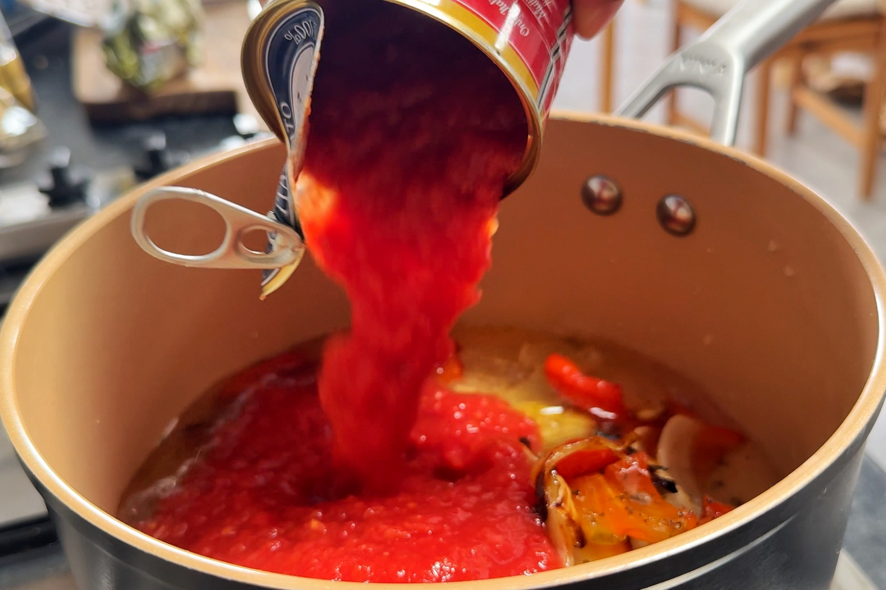 Pouring tinned tomatoes into a pan of good soup.