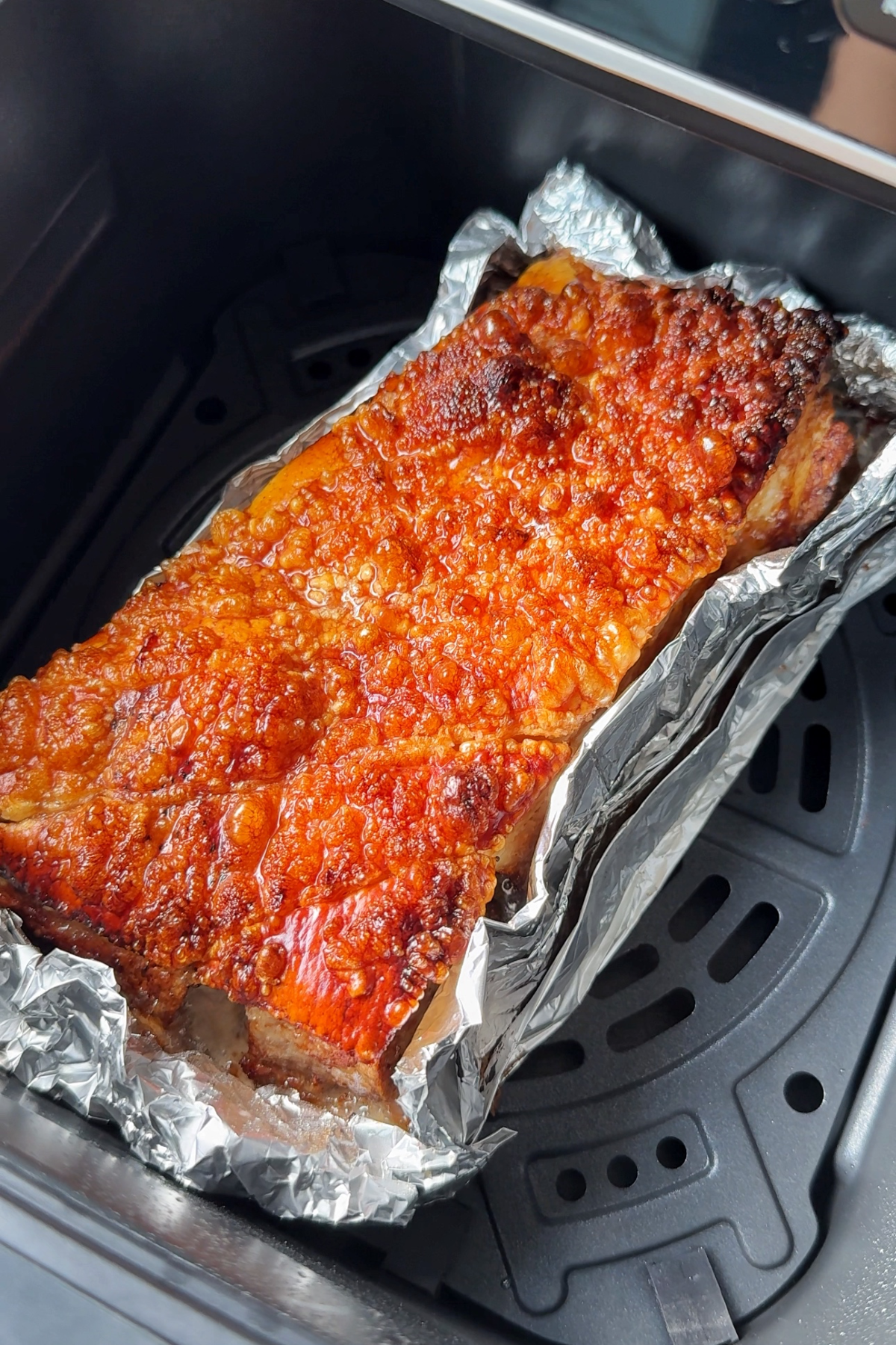 Air fryer pork belly with tinned foil wrapped around it. 