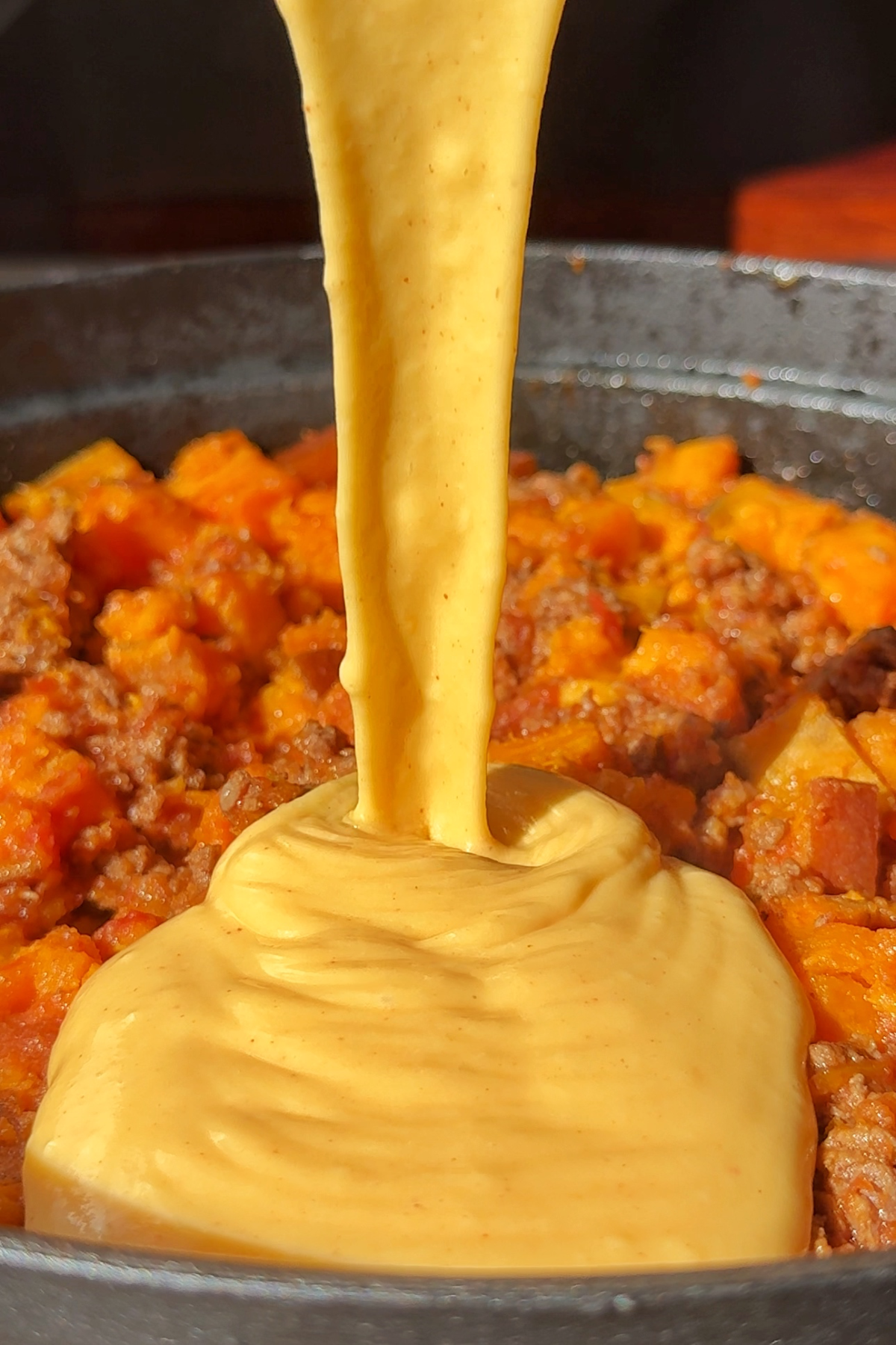Pouring cheese sauce over the sweet potato and ground beef.