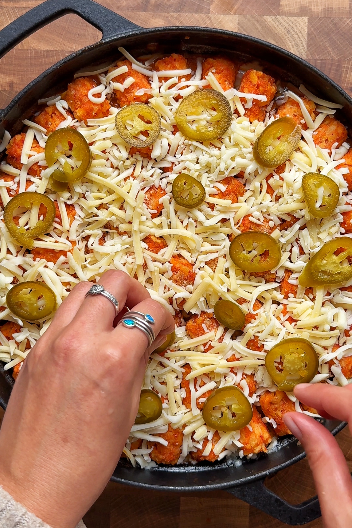 Sprinkling cheese and jalapeรฑos over the cowboy casserole.