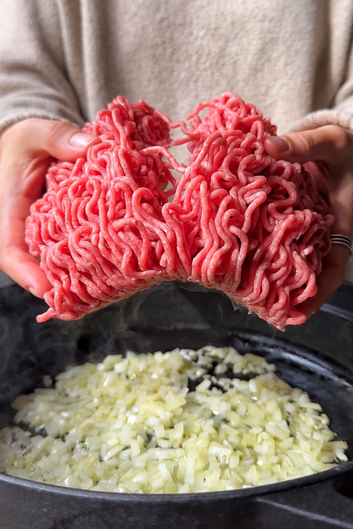 Breaking apart ground beef and placing it into a skillet with onion.