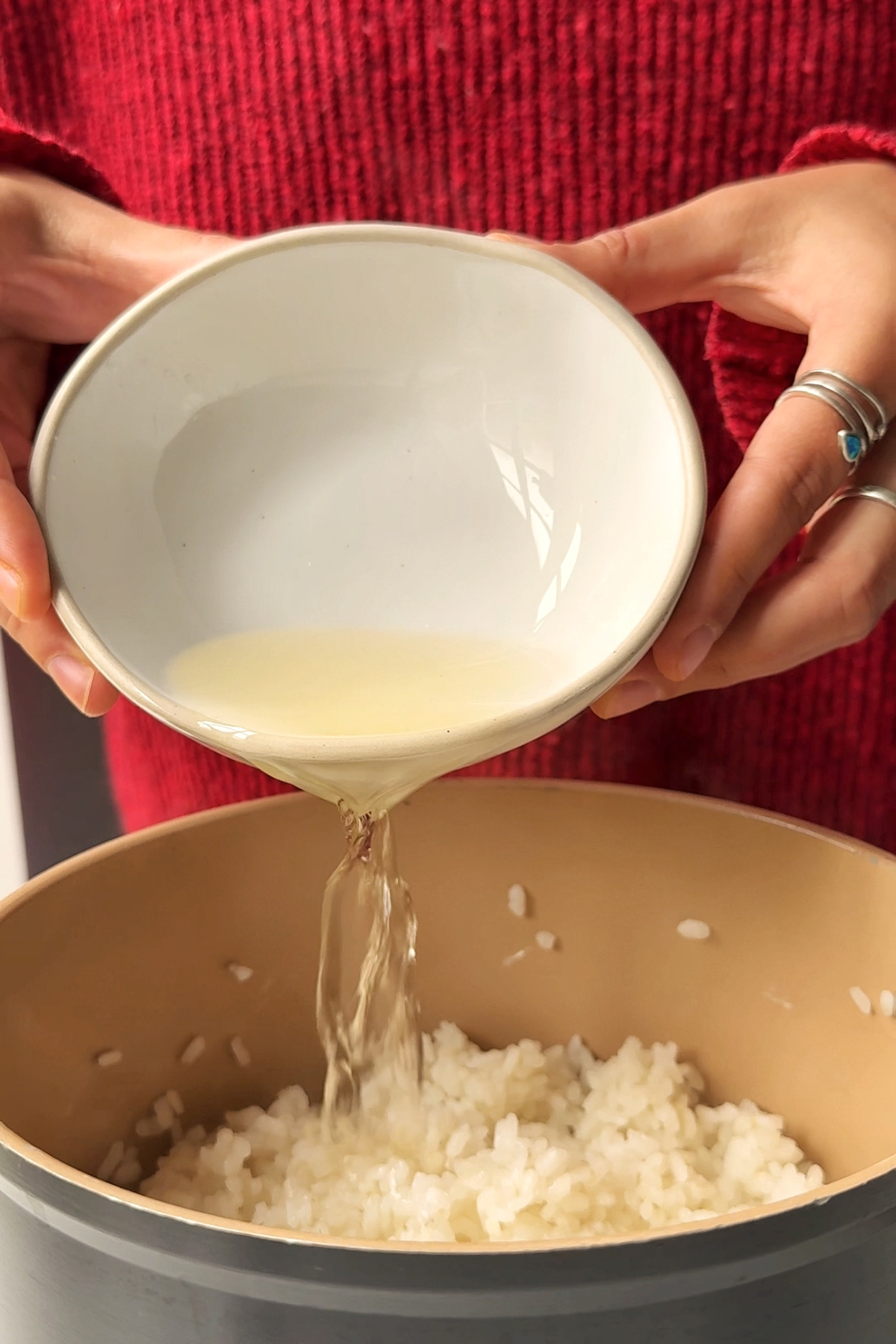 Pouring rice wine vinegar mixture into sushi rice.
