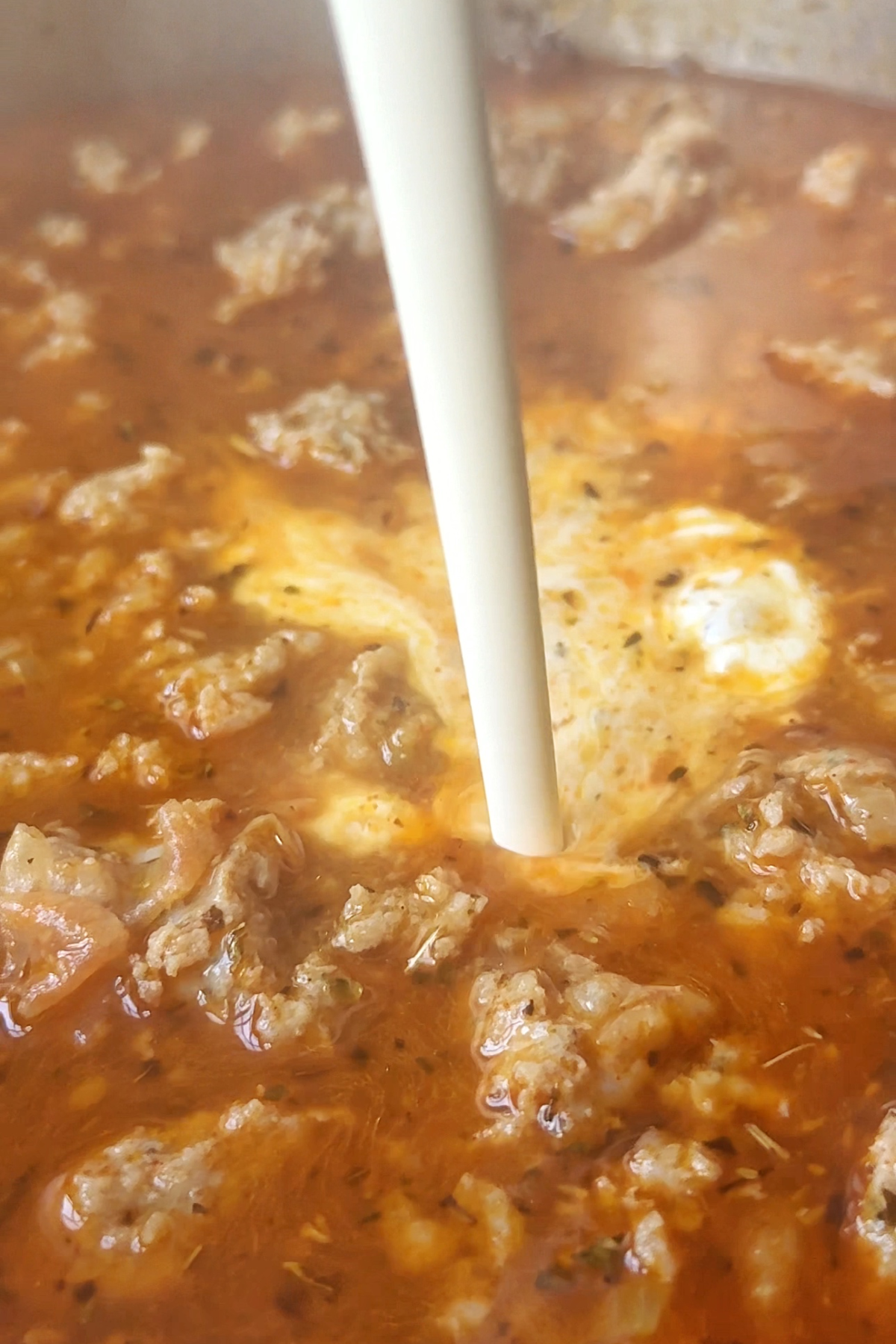 Pouring cream into the sausage kale white bean soup.