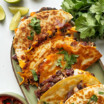 Bean tacos stacked on a green platter.