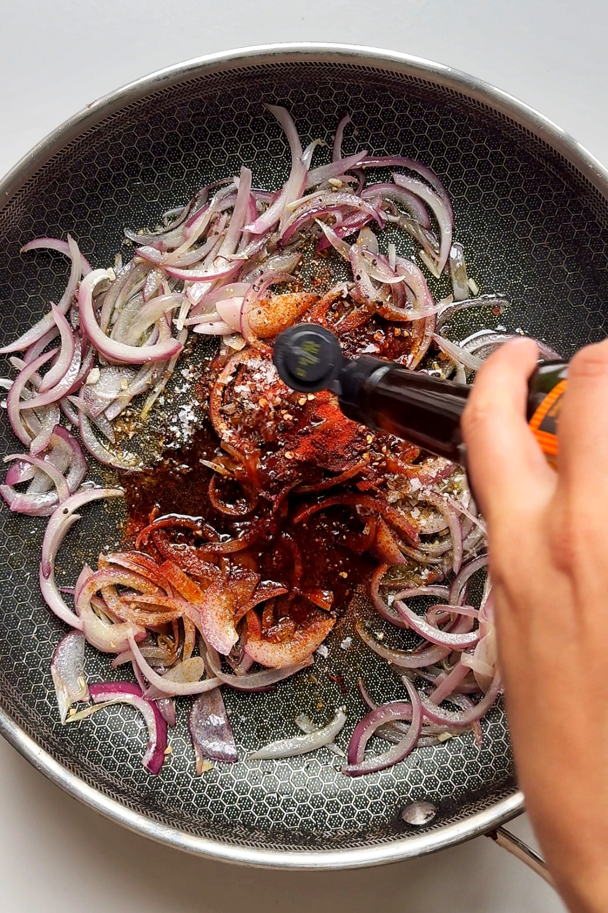 Adding seasonings to the pan with red onions, and garlic.