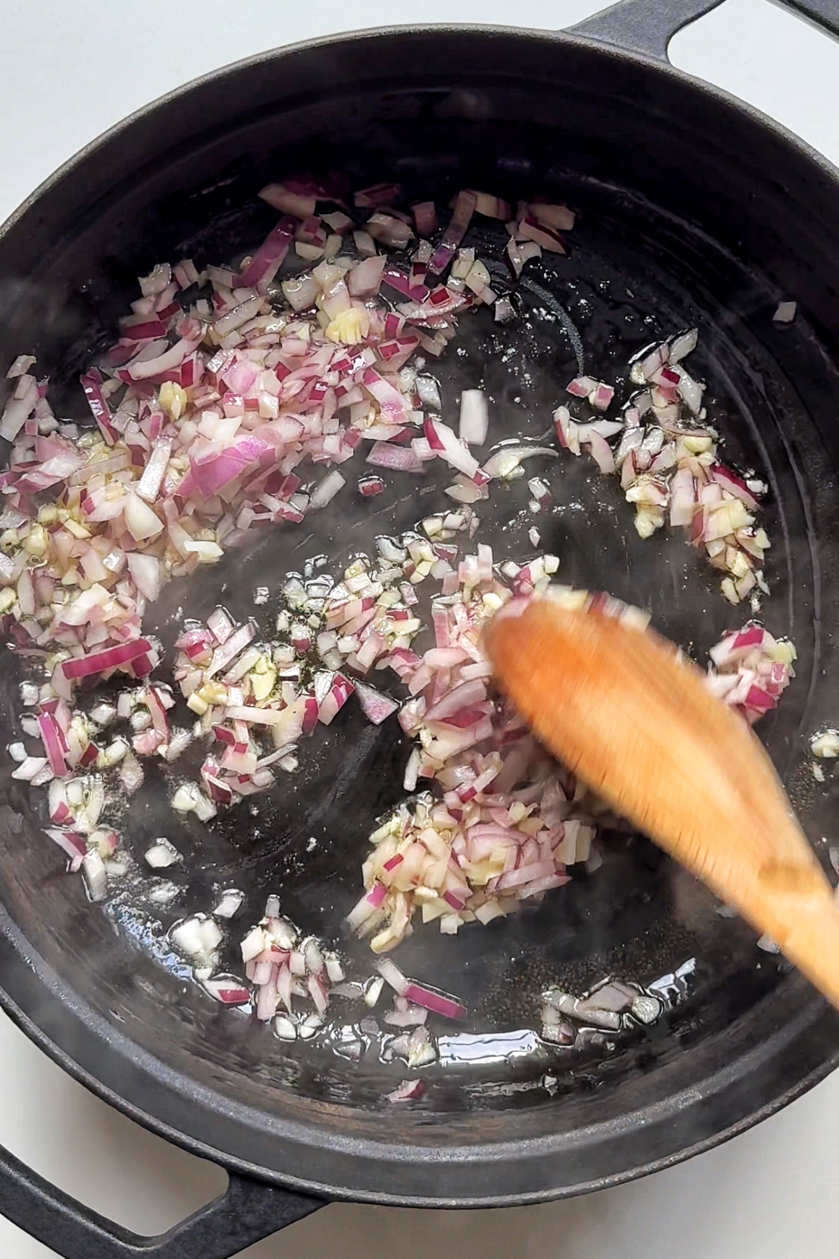 Frying garlic and onion in a black casserole dish.