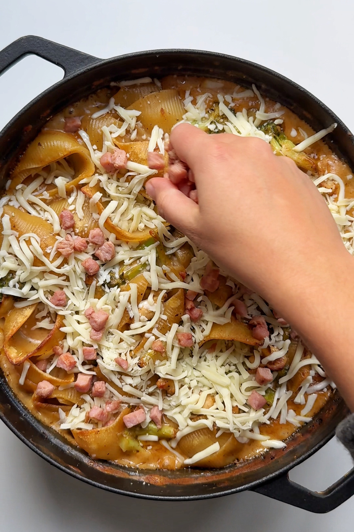 Topping chicken and broccoli pasta bake with cheese and lardons.