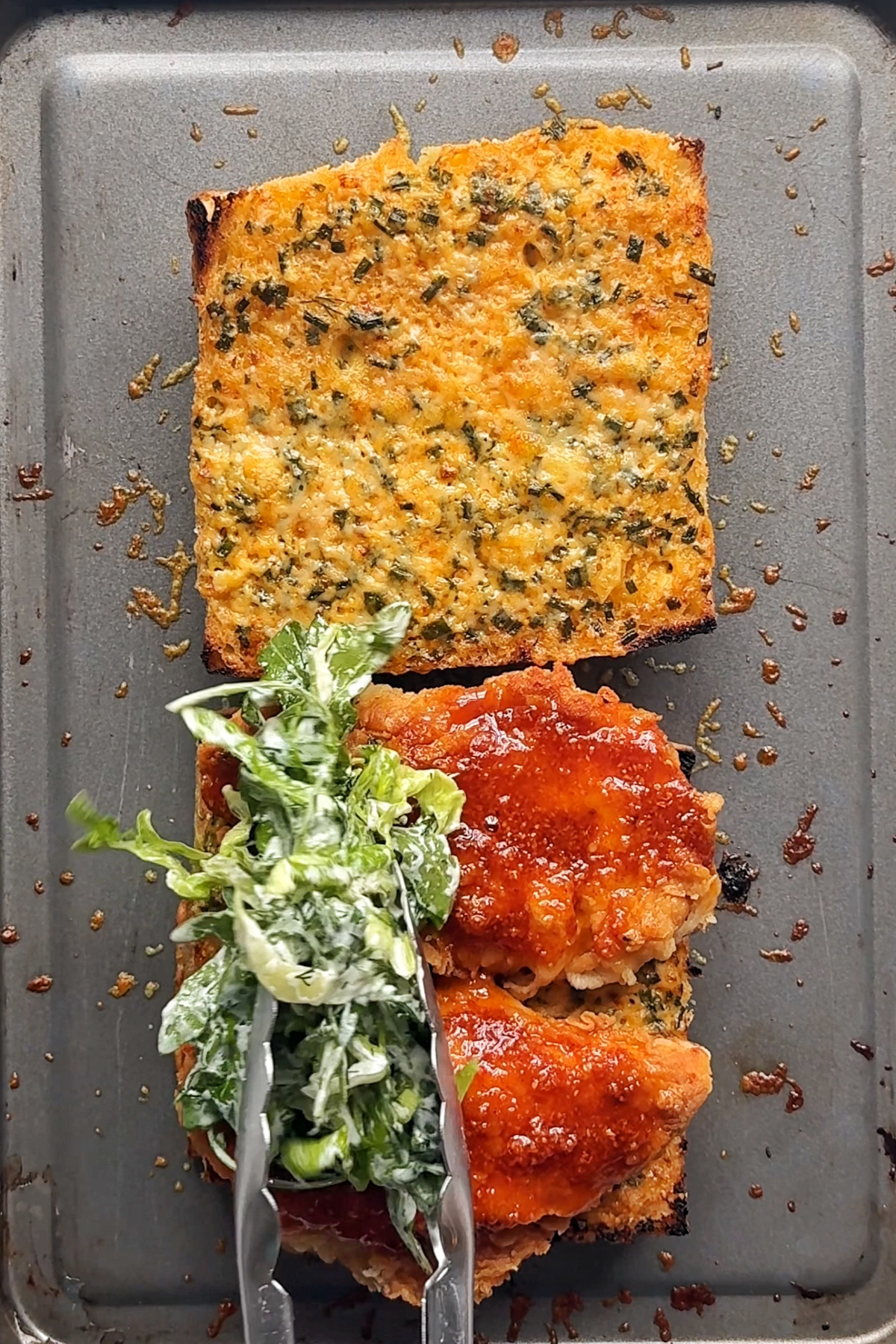 Placing salad on top of a hot honey chicken sandwich.