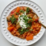 Sausage stew in a bowl topped with sour cream and parsley.