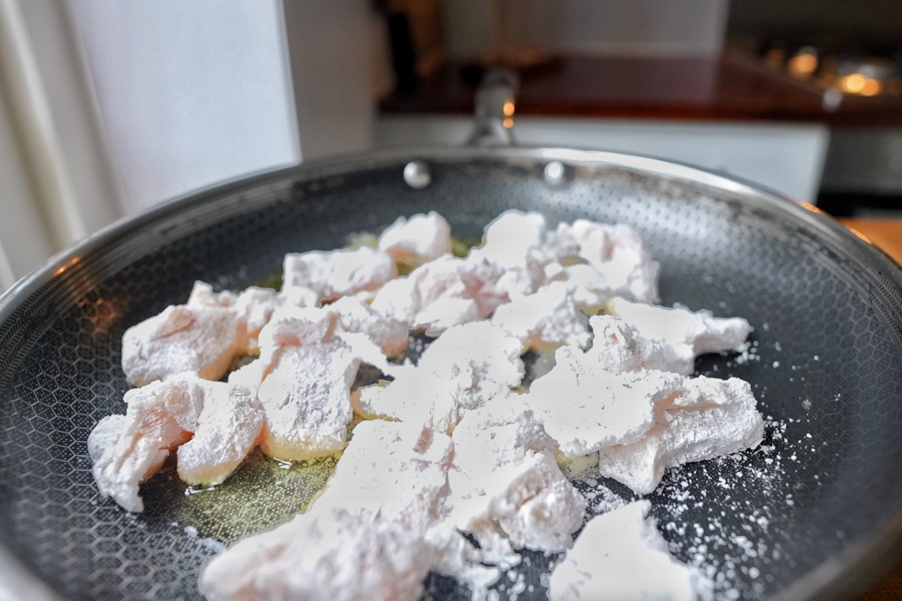 Coated chicken in cornflour frying in a pan.