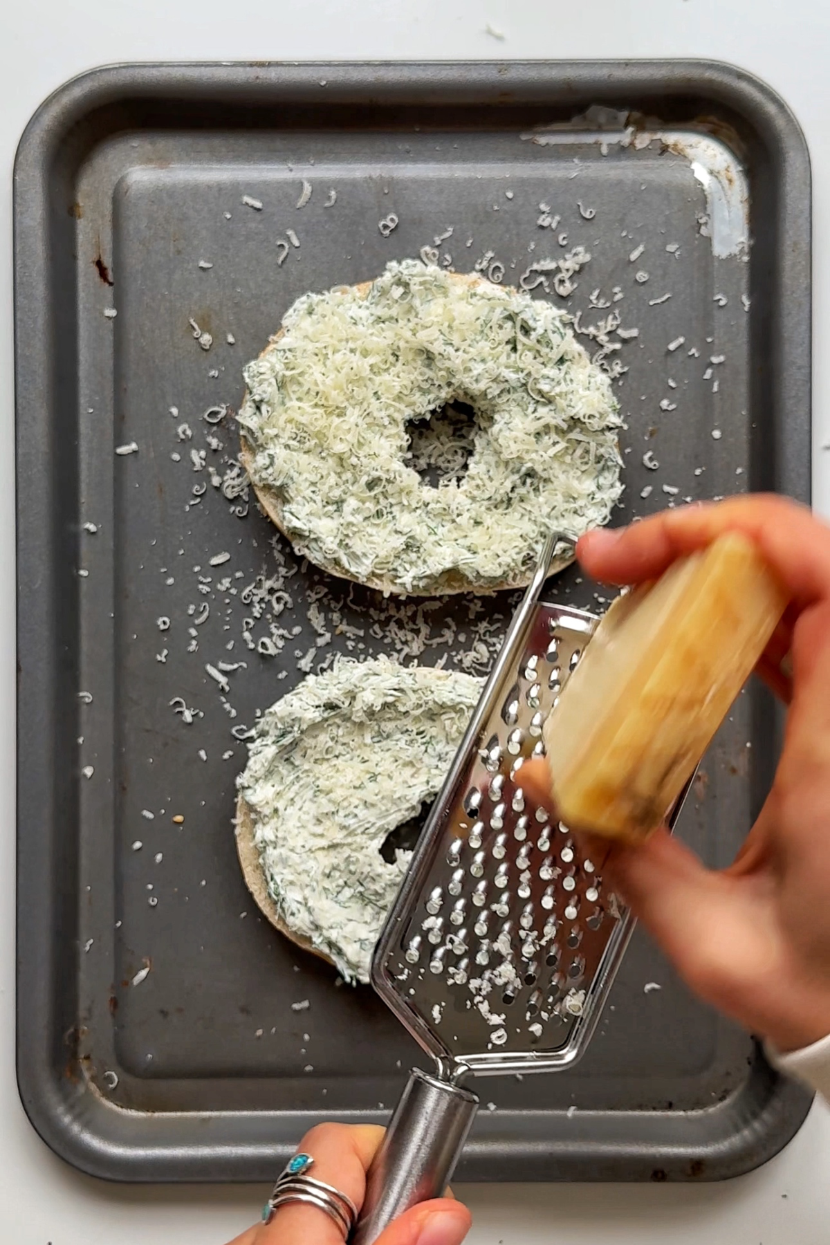 Grating parmesan onto bagels.