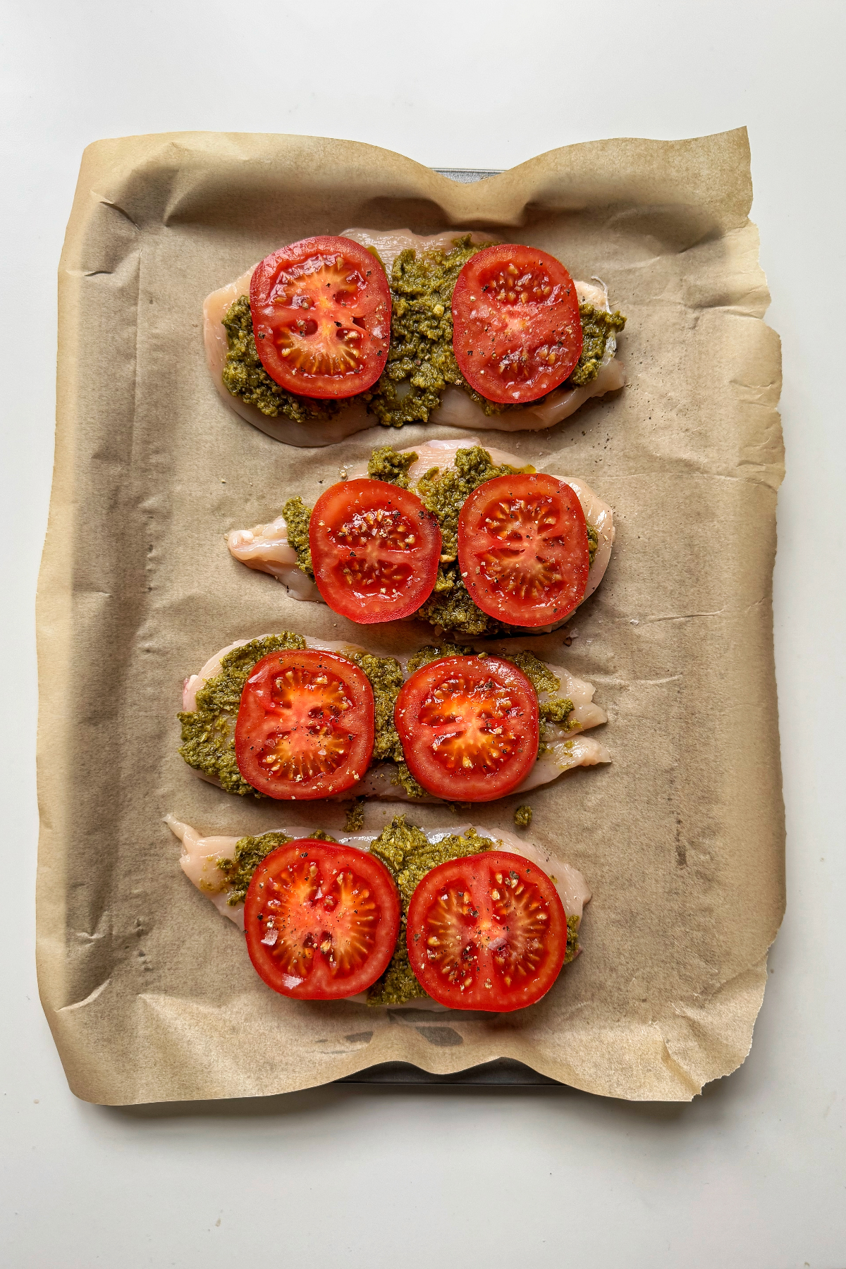 Placing pesto and tomato on sliced chicken breast.