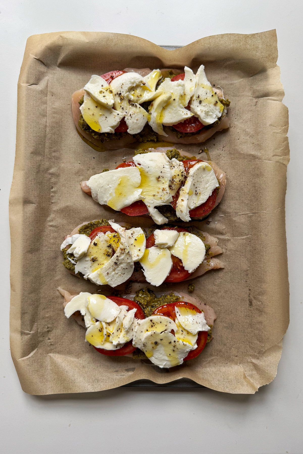 Mozzarella and tomato and pesto on top of chicken breast on a tray.