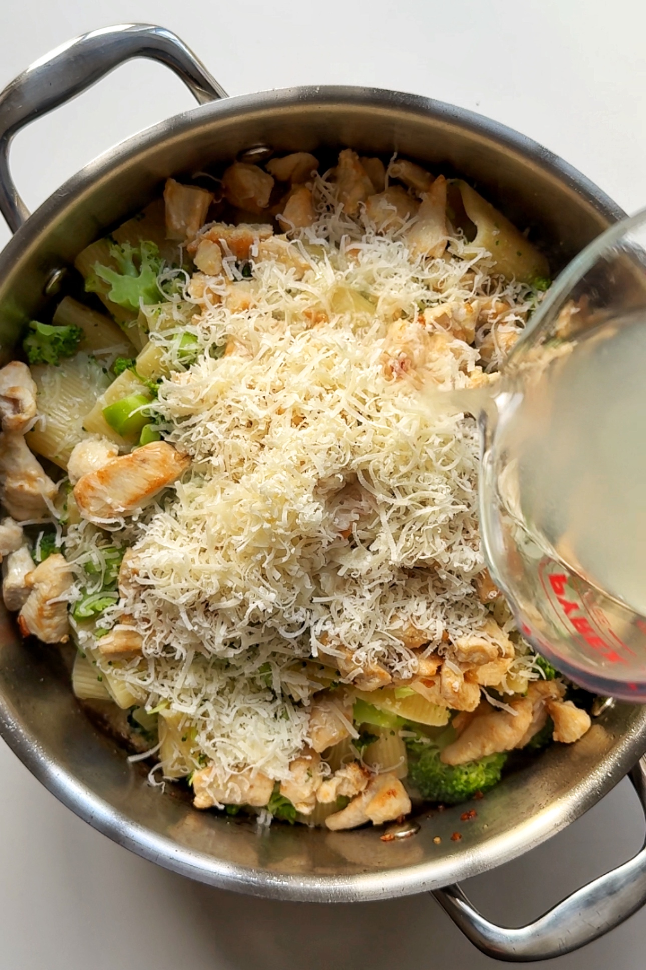 Combining the chicken, pasta, alfredo sauce, and broccoli in the pan.