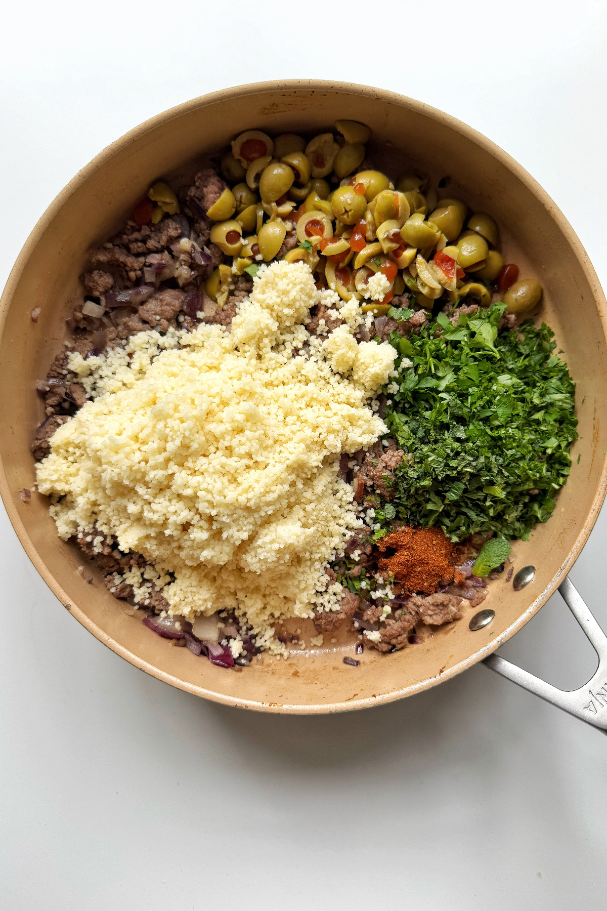 Combining ground turkey with couscous, parsley, mint, and olives in a pan.
