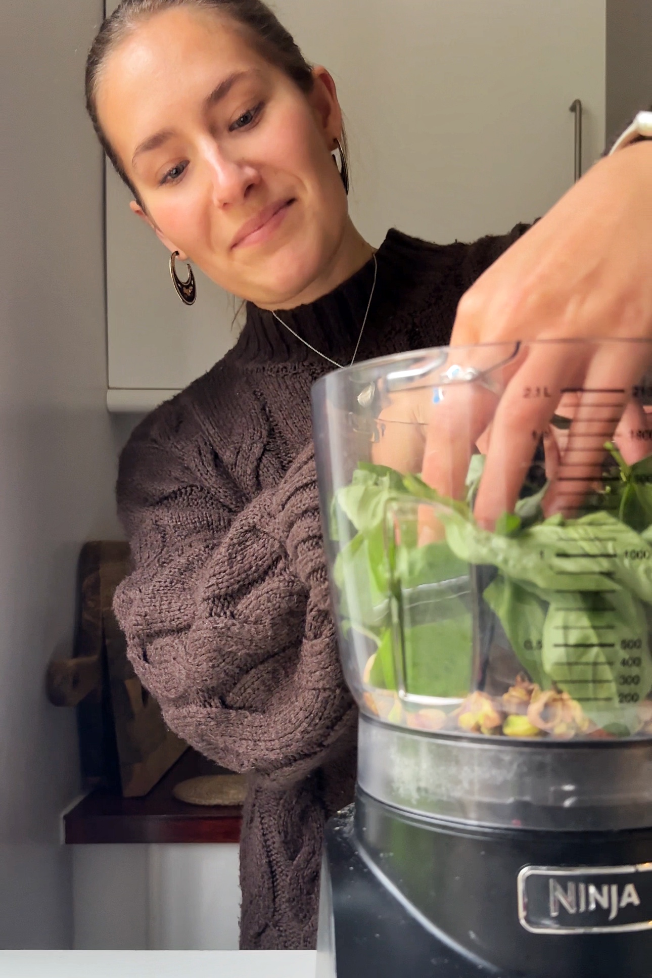 Combining basil, pistachios, and garlic to make pistachio pesto in food processor.
