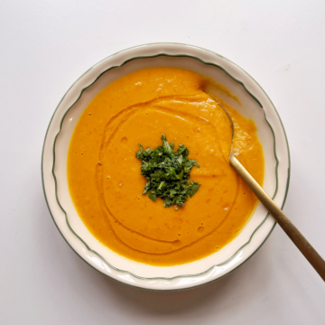 Carrot and ginger soup in white bowl with golden spoon.