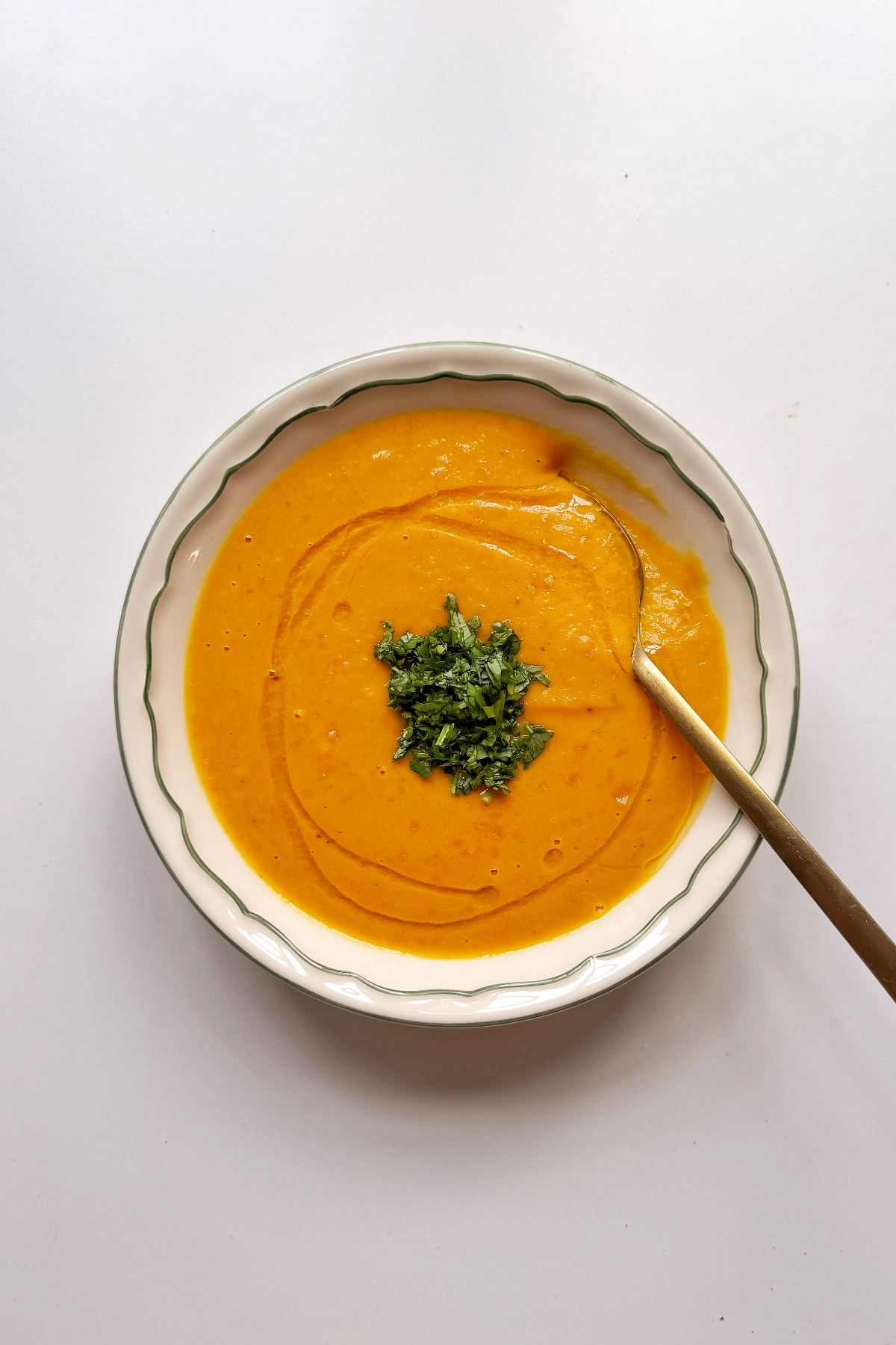 Carrot and ginger soup in white bowl with golden spoon.
