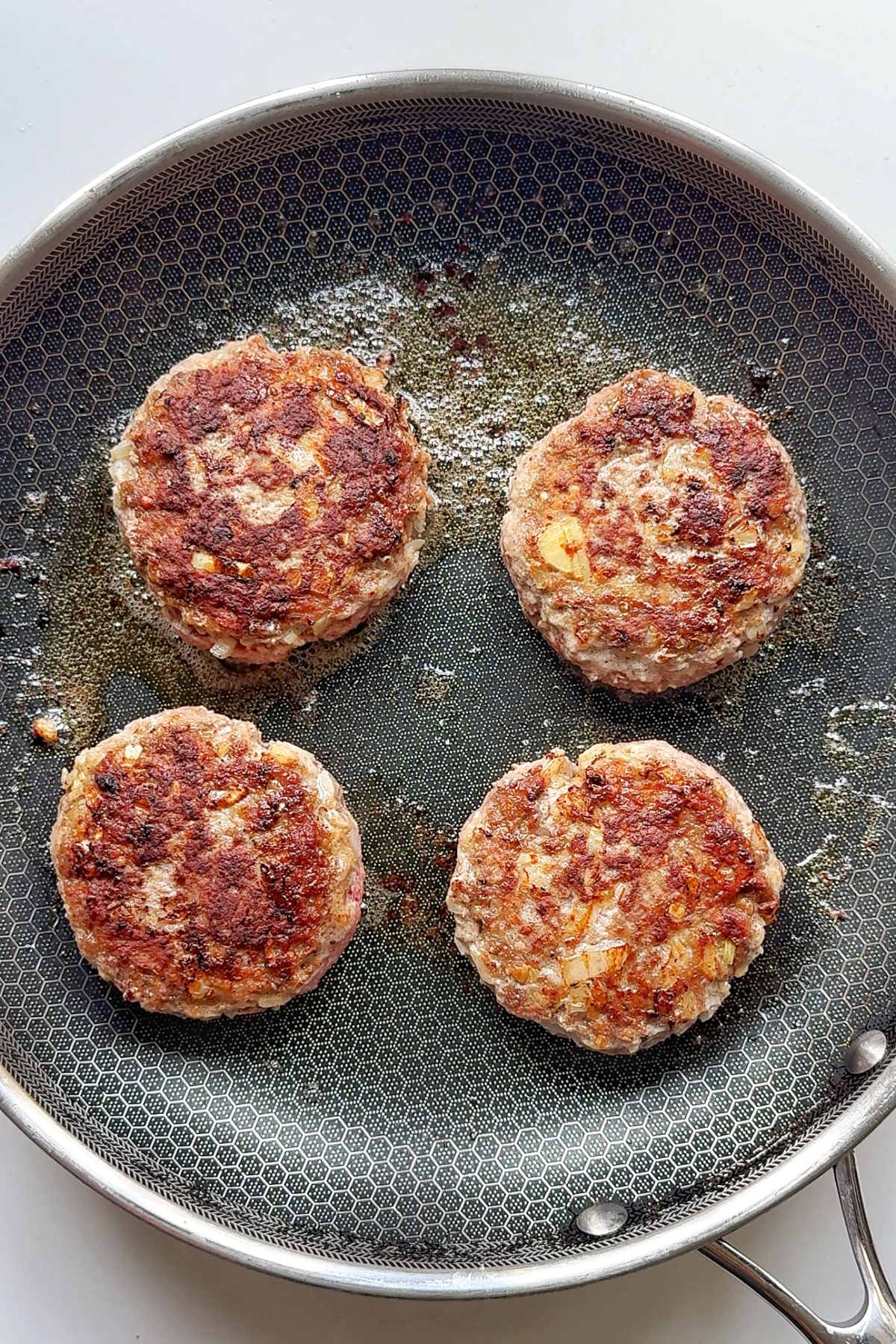 Frying beef patties in a metal skillet.