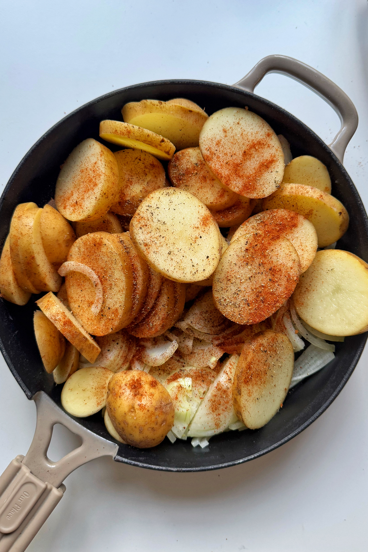 Adding potatoes and onions into a skillet.