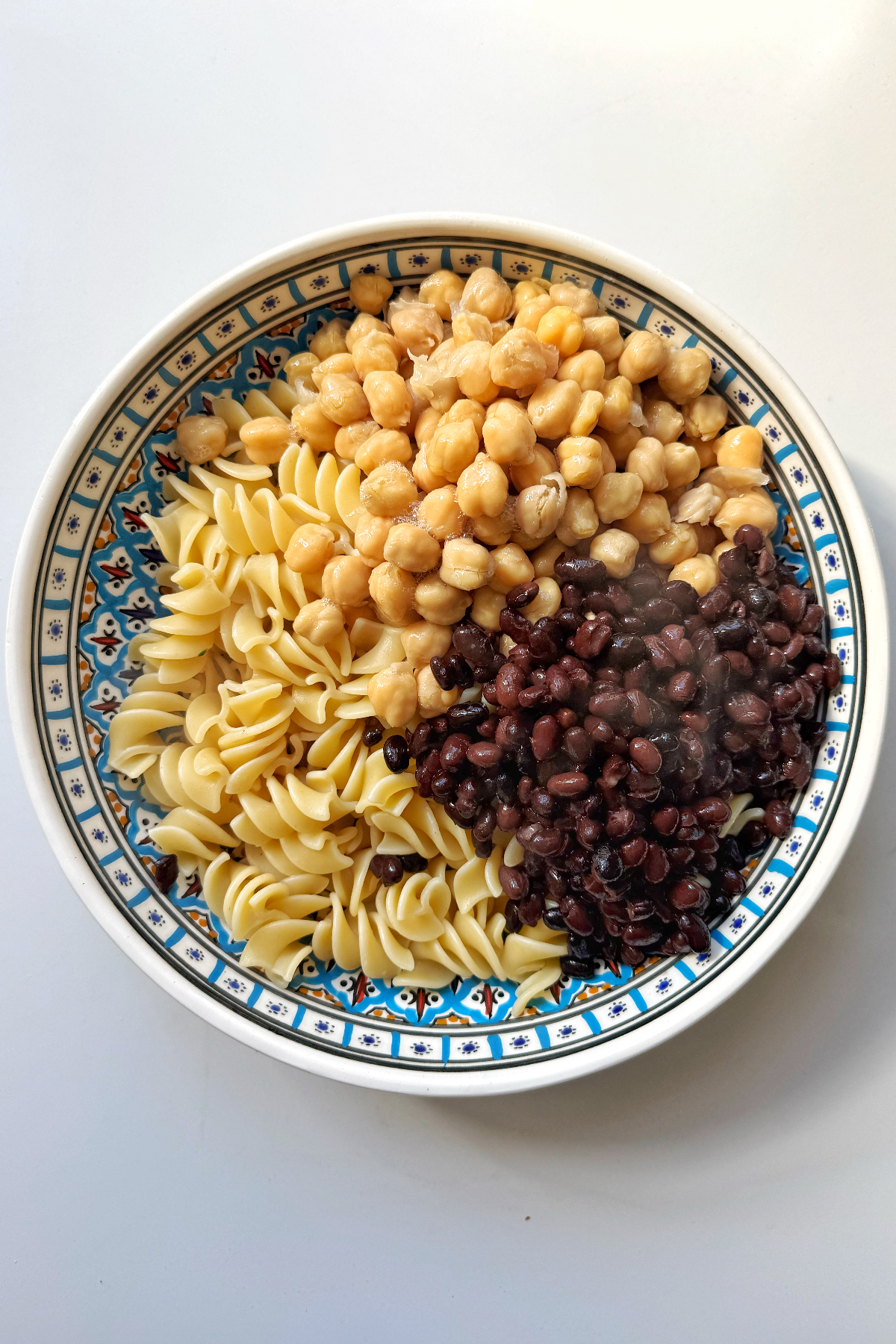 Adding beans to the pasta salad dish.